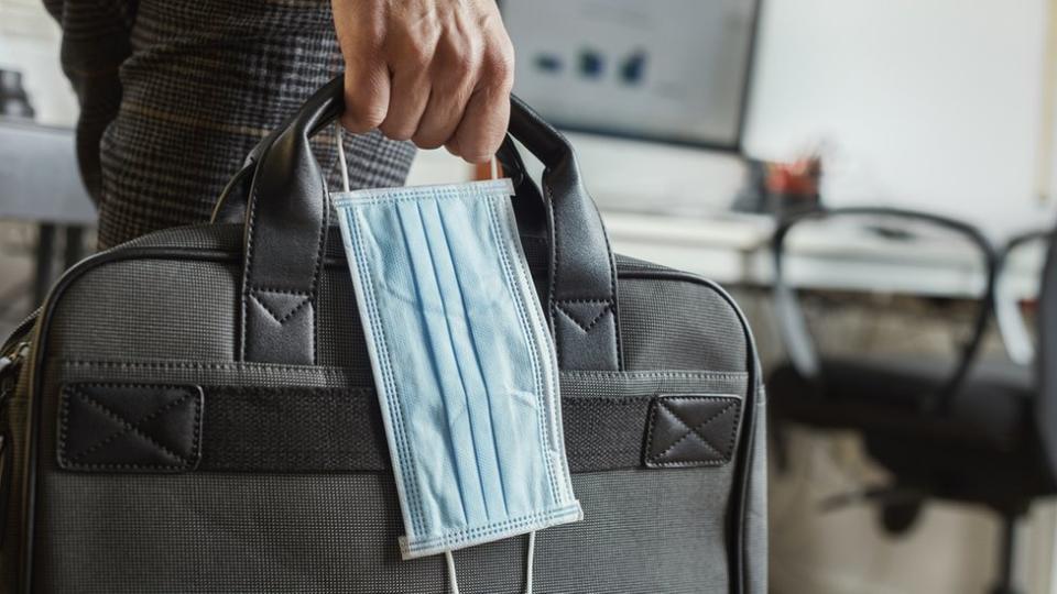 Un hombre lleva una mochila para laptop y una mascarilla.