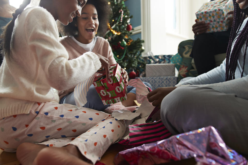 Happy sisters opening Christmas presents while sitting in living room at home