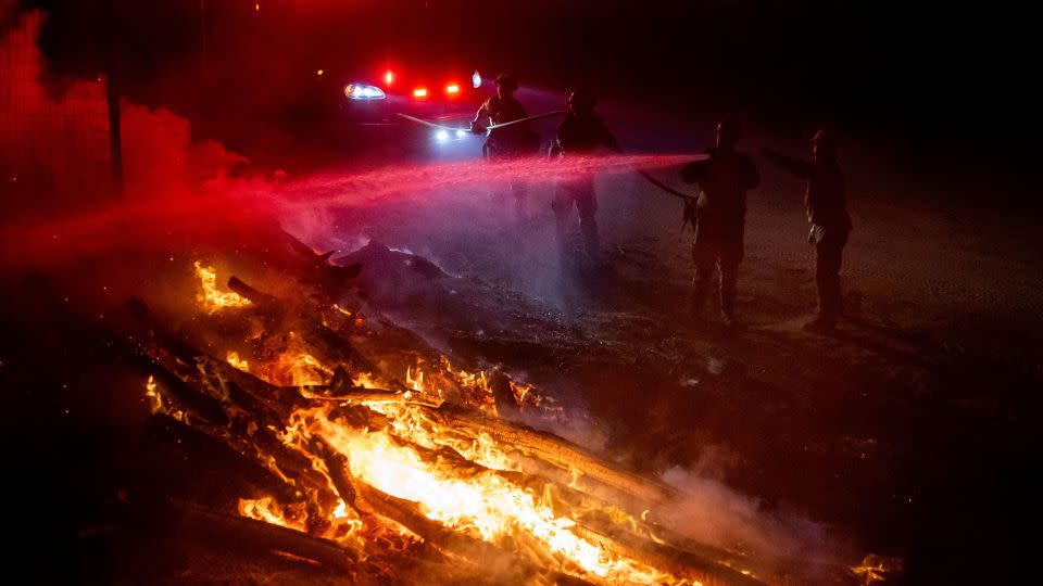 Firefighters douse flames while battling a wildfire called the Highland Fire in Aguanga, California, on Monday, October 30. - Ethan Swope/AP