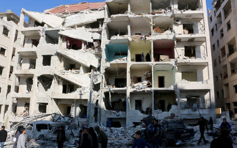 People inspect the damaged buildings after explosions were carried out with bomb-laden vehicles in Idlib, Syria  - Credit: Getty