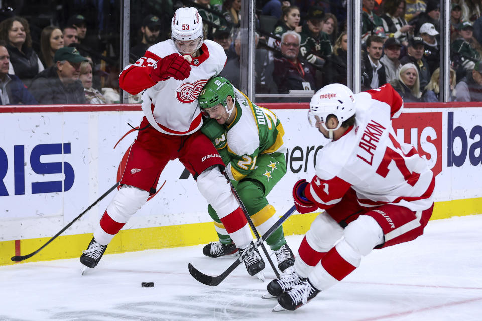 Detroit Red Wings defenseman Moritz Seider, left, and center Dylan Larkin (71) and Minnesota Wild right wing Brandon Duhaime, middle, compete for the puck during the second period of an NHL hockey game Wednesday, Dec. 27, 2023, in St. Paul, Minn. (AP Photo/Matt Krohn)