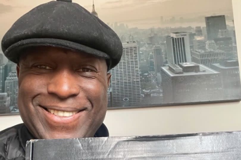 Kevin Campbell posing with a picture of some food products while wearing a flat cap