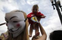 A woman, wearing a Guy Fawkes mask, holds up a homeless child during a Christmas street celebration in downtown Sao Paulo December 24, 2013. Members of the Black Bloc group and the Anonymous movement provided food and clothes to homeless people during the celebration. REUTERS/Nacho Doce (BRAZIL - Tags: SOCIETY)