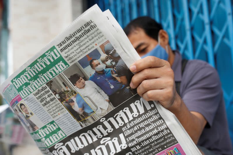 A supporter of Parit Chiwarak, reads a newspaper in front of a police station as he waits for Parit to be sent to court in Bangkok