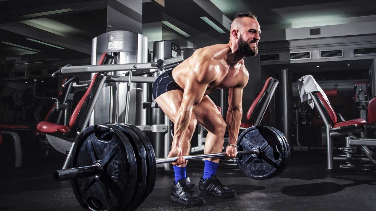  Man in the gym attempting a heavy deadlift using a barbell with several plates on each end 