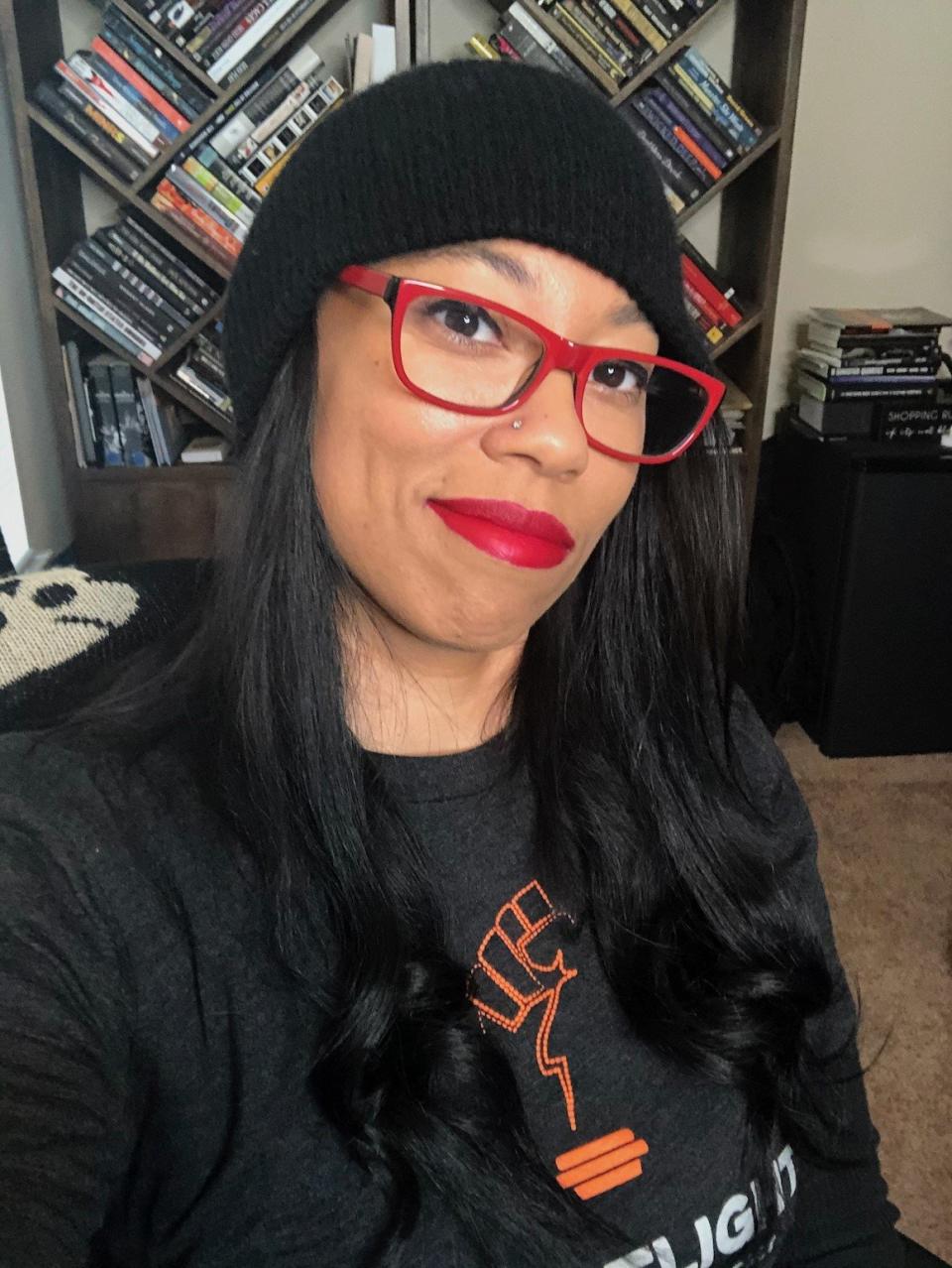 Tonia Ransom of Nightlight Podcast wears a black hat, red rimmed glasses and lipstick, and a nightlight podcast shirt.