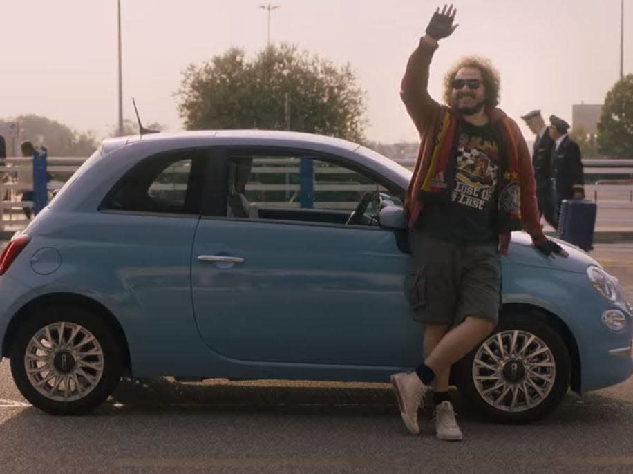 umberto standing in front of a small blue car in love in the villa