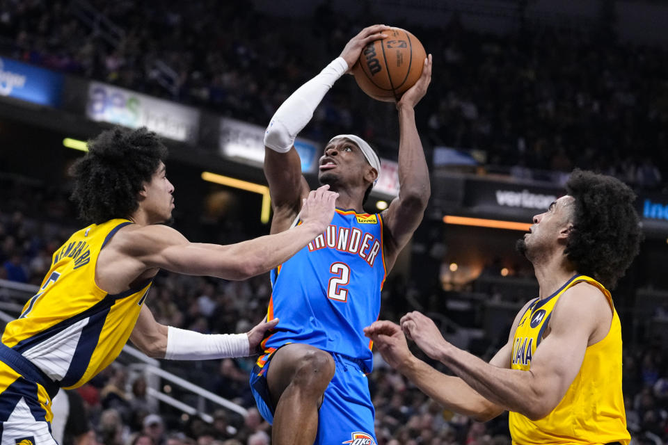 Oklahoma City Thunder guard Shai Gilgeous-Alexander (2) shoots between Indiana Pacers guard Andrew Nembhard, left, and forward Jordan Nwora during the first half of an NBA basketball game in Indianapolis, Friday, March 31, 2023. (AP Photo/Michael Conroy)