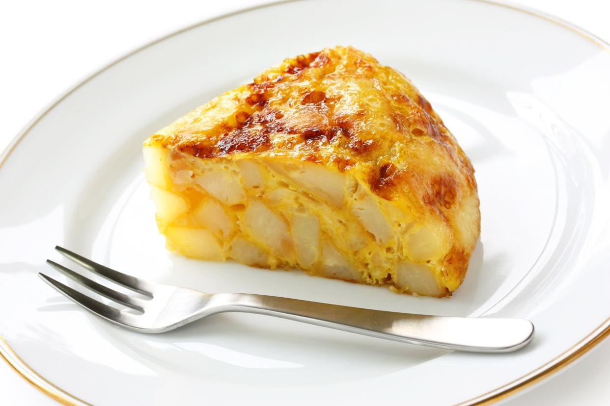 Spanish potato omelet on a porcelain plate with a dessert fork with a white background