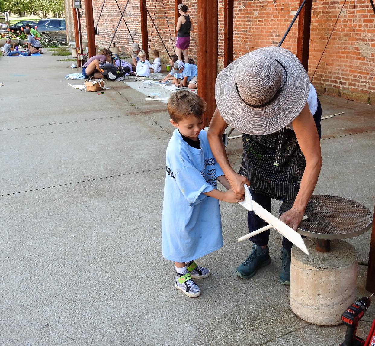 Sawyer Farley, 4, helps Anne Cornell of the Pomerene Center for the Arts cut plastic pipe to help make a fish puppet during youth programming at the artPARK.