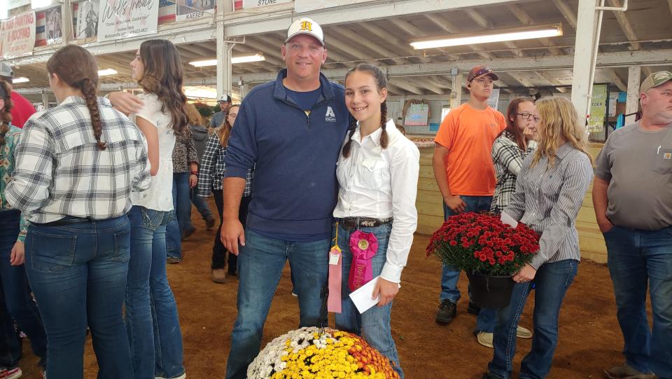 Ava Buzzard and her dad, Chad Buzzard, are ready to give the buyer of her market hog, Tommy, a colorful autumn mum on Friday morning at the Ashland County Fair. They said they got attached to Tommy in caring for him.