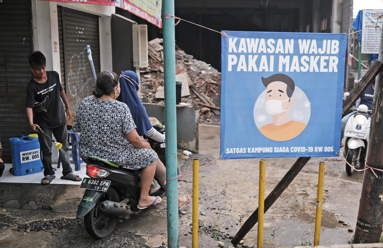 A man sprays disinfectant at motorists near a banner calling for people to wear their mask as a precaution against the new coronavirus outbreak, at a small road leading to a neighborhood in Jakarta, Indonesia, Tuesday, May 12, 2020. Writings on the banner read "Wear mask beyond this point". (AP Photo/Dita Alangkara)