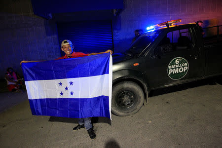 A Honduran holds a flag of Honduras in front of a military vehicle before leaving with a new caravan of migrants, set to head to the United States, at a bus station in San Pedro Sula, Honduras January 14, 2019. REUTERS/Jorge Cabrera