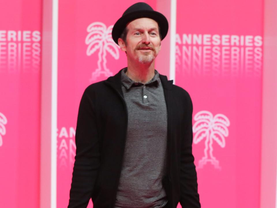 Denis O'hare in 2020 wearing a black hat in front of pink background