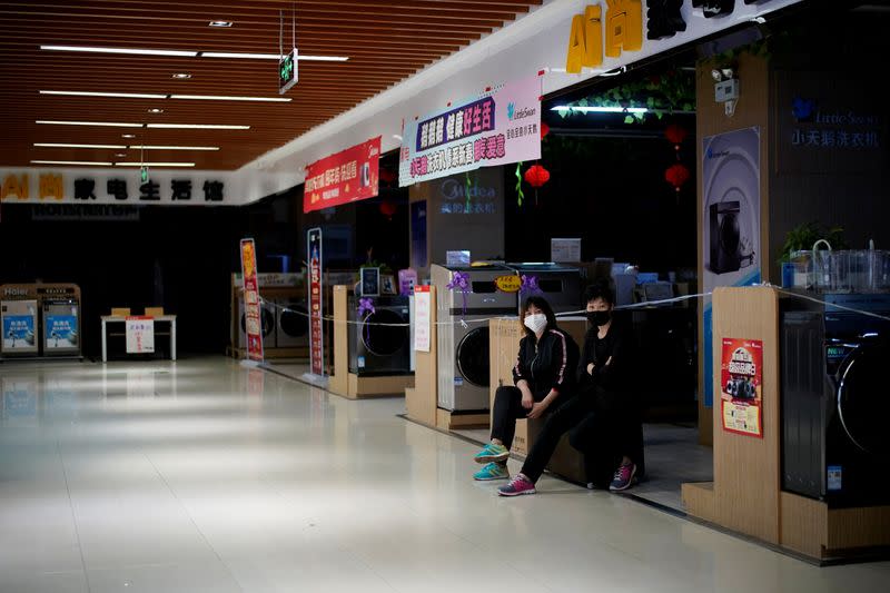 FILE PHOTO: Women wearing face masks wait for customers at an electrical appliances store in Xianning