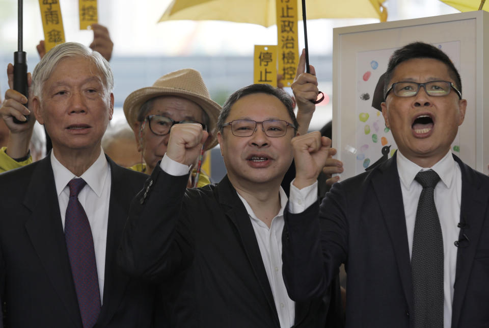 Occupy Central leaders, from right, Chan Kin Man, Benny Tai and Chu Yiu Ming shout slogans before entering a court in Hong Kong, Monday, Nov. 19, 2018. Nine leaders of the 2014 Hong Kong pro-democracy movement stand trial today. The co-founders of the "Occupy Central" campaign - legal Professor Benny Tai Yiu-Ting, sociology professor Chan Kin-man and retired pastor Chu Yiu-ming - are facing charges related to the planning and implementation of the campaign which became part of the large-scale pro-democracy Umbrella Movement protests which were carried out 79 days between September and December 2014. (AP Photo/Vincent Yu)