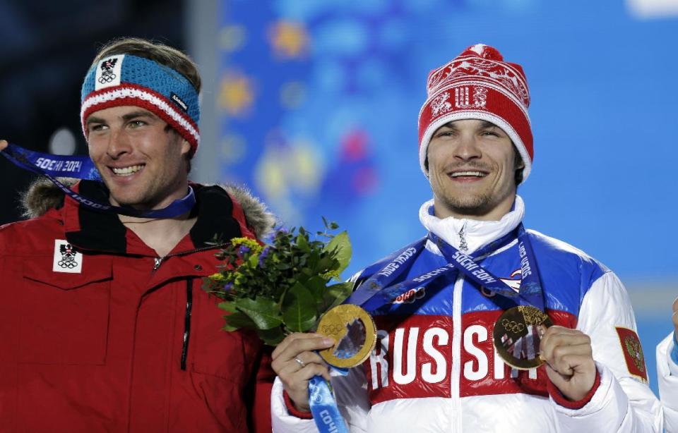 Austria's Benjamin Karl, the bronze medalist in the men's snowboard parallel slalom, left, smiles while standing next to gold medalist Vic Wild of Russia, who also won the gold medal in the men's snowboard parallel giant slalom, during their medals ceremony at the 2014 Winter Olympics, Saturday, Feb. 22, 2014, in Sochi, Russia. (AP Photo/David Goldman)