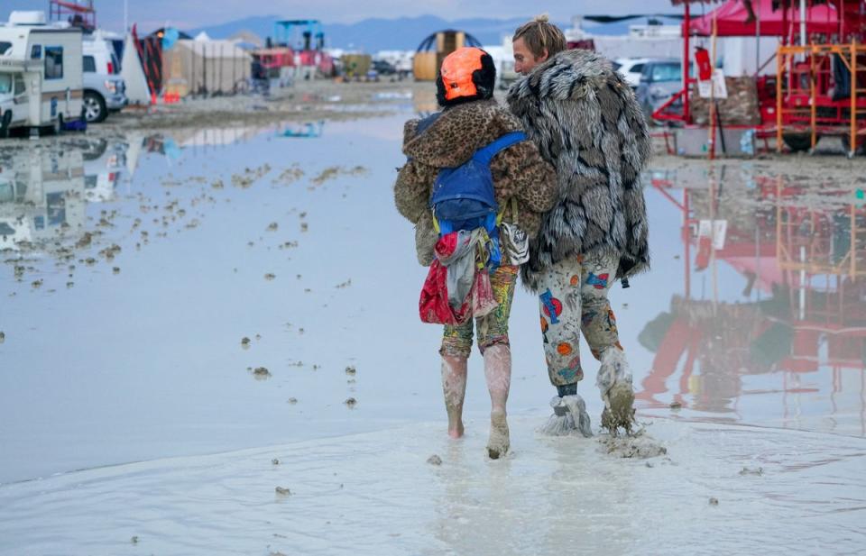 Dub Kitty and Ben Joos, of Idaho and Nevada, walk through the mud at Burning Man after a night of dancing with friends (via REUTERS)