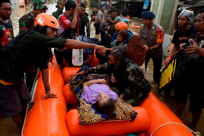 An elderly woman is being evacuated on an inflatable boat by a rescue team, after floods hit a residential area in Bekasi