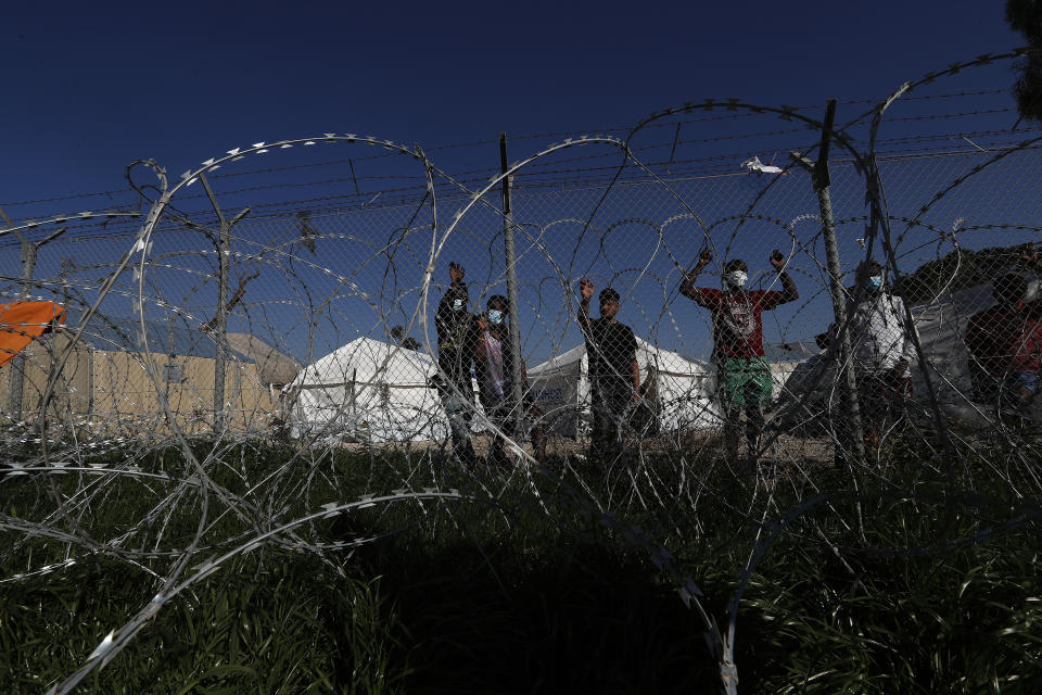 Migrants stand behind a fence inside a refugee camp in Kokkinotrimithia outside of capital Nicosia, Cyprus, Friday, Feb. 5, 2021. Cyprus' Interior Minister Nicos Nouris said this week that the east Mediterranean island nation whose closest point to Syria is around 150 kilometers (93 miles) remains first among all other European Union member states with the most asylum applications relative to its population. Last year, the country of around 1.1 million people racked up 7,000 asylum applications - most of them from Syrians. (AP Photo/Petros Karadjias)