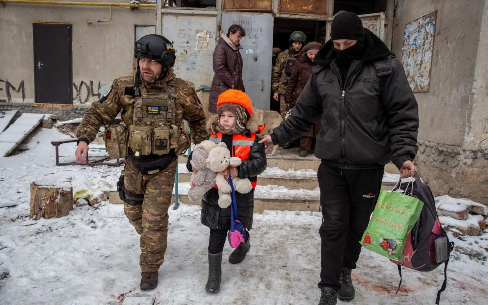 Policemen help Arina, 6, dressed in children's bulletproof vest and helmet during her evacuation from front line city of Bakhmut - STRINGER/REUTERS