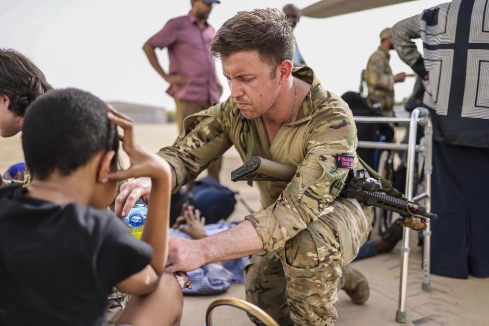 In this handout image provided by the UK Ministry of Defence, on Thursday, April 27, 2023, a Royal Marine looks after an evacuee whilst waiting for an aircraft bound for Cyprus, at Wadi Seidna military airport, 22 kilometres (14 mi) north of Khartoum, Sudan. (PO Phot Aaron Hoare/UK Ministry of Defence via AP)