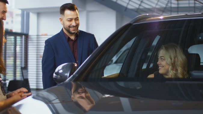 Consultant helping woman and kids to get inside of new car while testing it in dealer shop.