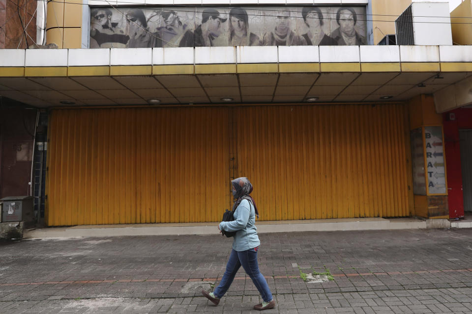 In this Thursday, April 30, 2020, photo, a woman walks past a shop closed due to the new coronavirus outbreak at Pasar Baru Shopping Center that is popular for its textiles products in Jakarta, Indonesia. May Day usually brings both protest rallies and celebrations rallies marking international Labor Day. This year it's a bitter reminder of how much has been lost for the millions left idle or thrown out of work due to the coronavirus pandemic. Garment workers in Asia are among the hardest hit as orders dry up and shutdowns leave factories shuttered. (AP Photo/Tatan Syuflana)