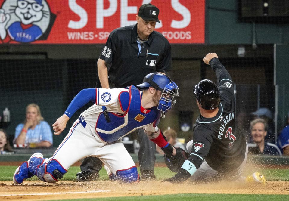 Texas Rangers catcher Jonah Heim tags out Arizona Diamondbacks' Joc Pederson (3) at home plate, while umpire Todd Tichenor watches during the sixth inning of a baseball game Tuesday, May 28, 2024, in Arlington, Texas. Pederson was originally called safe on the play, but the call was overturned. (AP Photo/Jeffrey McWhorter)