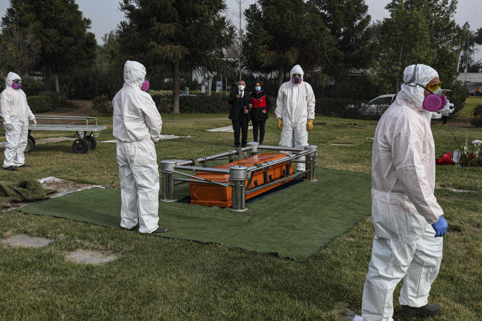 Trabajadores de un cementerio con equipo para protegerse del coronavirus observan tras cargar el ataúd de Mónica Lagos, de 72 años, el lunes 15 de junio de 2020 en el cementerio Manantial en Santiago, Chile. Según su nieta Ninoska Vásquez, Lagos falleció de complicaciones relacionadas con la enfermedad COVID-19. (AP Foto/Esteban Félix)