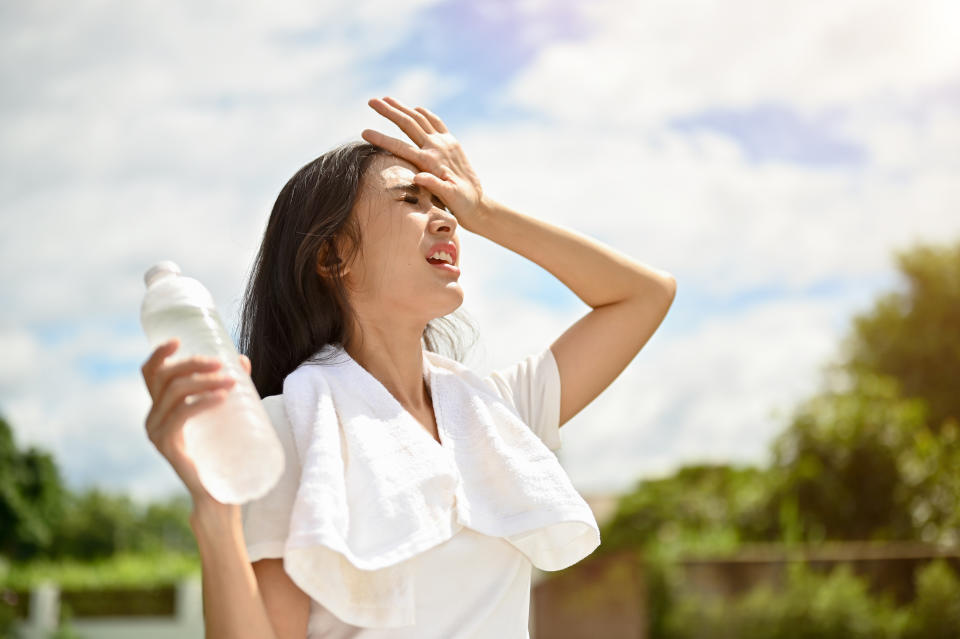 An exhausted and sweaty young Asian woman in sportswear is fighting the heat wave while running in a park on a sunny summer day. summer activity, heat stroke, dehydrated