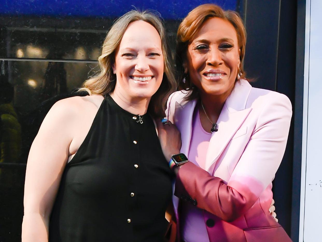 Amber Laign, in a black dress, and Robin Roberts, in a purple ombre suit, pose smiling together.