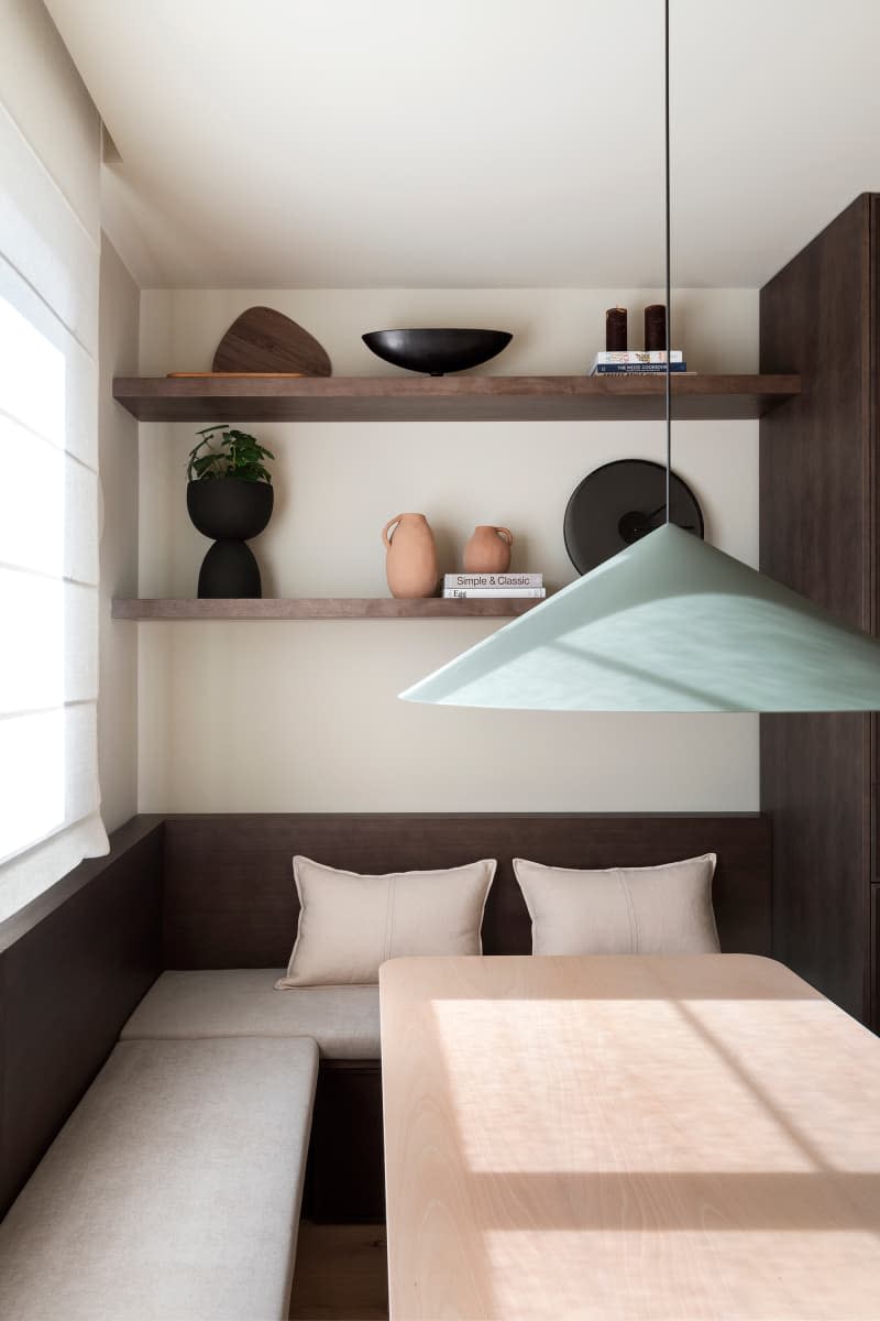 modern minimal white dining area with dark brown shelves and bench, and pale green pendant lamp