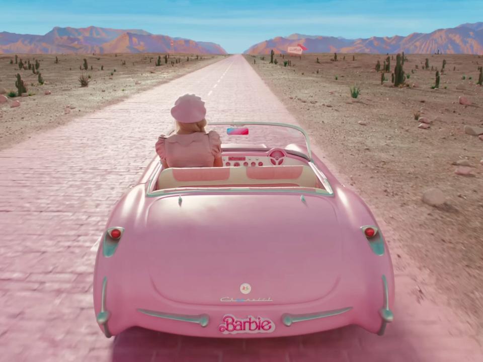 Margot Robbie as Barbie, driving along a pink brick road, in "Barbie."