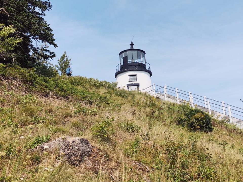 A black and white lighthouse peaking over the edge of a grassy hill