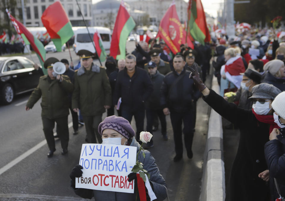 An opposition supporter holds placard reading "The best constitutional amendment is your resignation" in front of column of Belarusian President Alexander Lukashenko's supporters in Minsk, Belarus, Monday, Oct. 19, 2020. The elderly rallied in Minsk once again on Monday to demand resignation of the country's President Alexander Lukashenko, as mass protests triggered by a disputed election continue to rock Belarus. Lukashenko's older supporters also gathered in the country's capital Monday for a pro-government rally. (AP Photo)