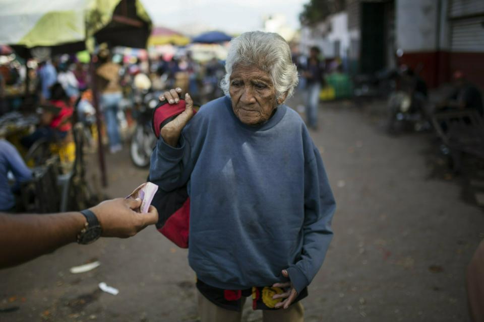 An elderly woman is offered cash as she begs at a wholesale food market in Caracas, Venezuela, Monday, Jan. 28, 2019. Economists agree that the longer the standoff between the U.S.-backed opposition leader Juan Guaido and President Nicolas Maduro drags on, the more regular Venezuelans are likely to suffer. (AP Photo/Rodrigo Abd)