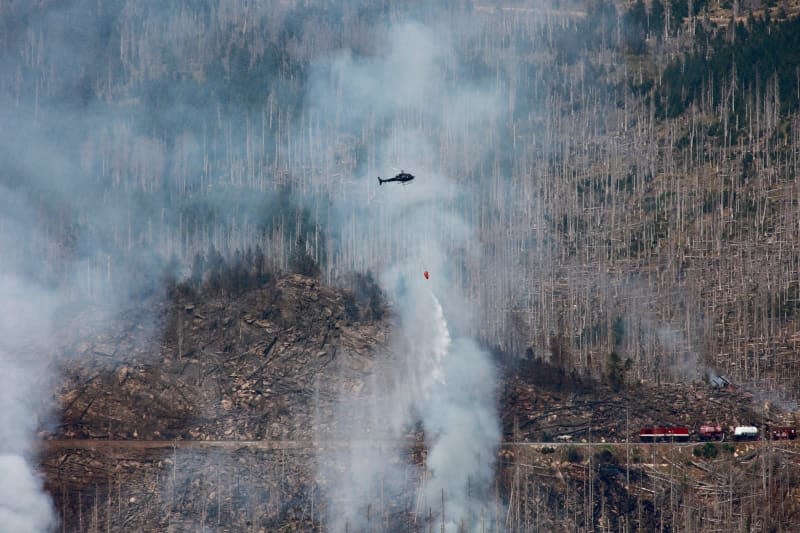 A fire-fighting helicopter flies over the Königsberg through thick clouds of smoke and drops water. The fire on the Brocken in the Harz mountains has spread further. Matthias Bein/dpa