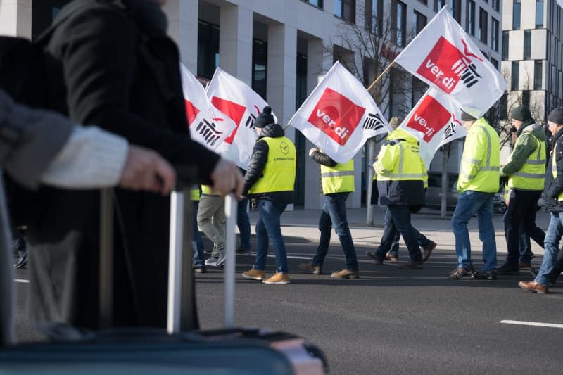 Strikers walk behind passengers during a Verdi rally at Berlin Brandenburg Airport. With renewed warning strikes by several professional groups, the Verdi trade union is paralyzing important parts of German air traffic on Thursday and Friday. Sebastian Gollnow/dpa