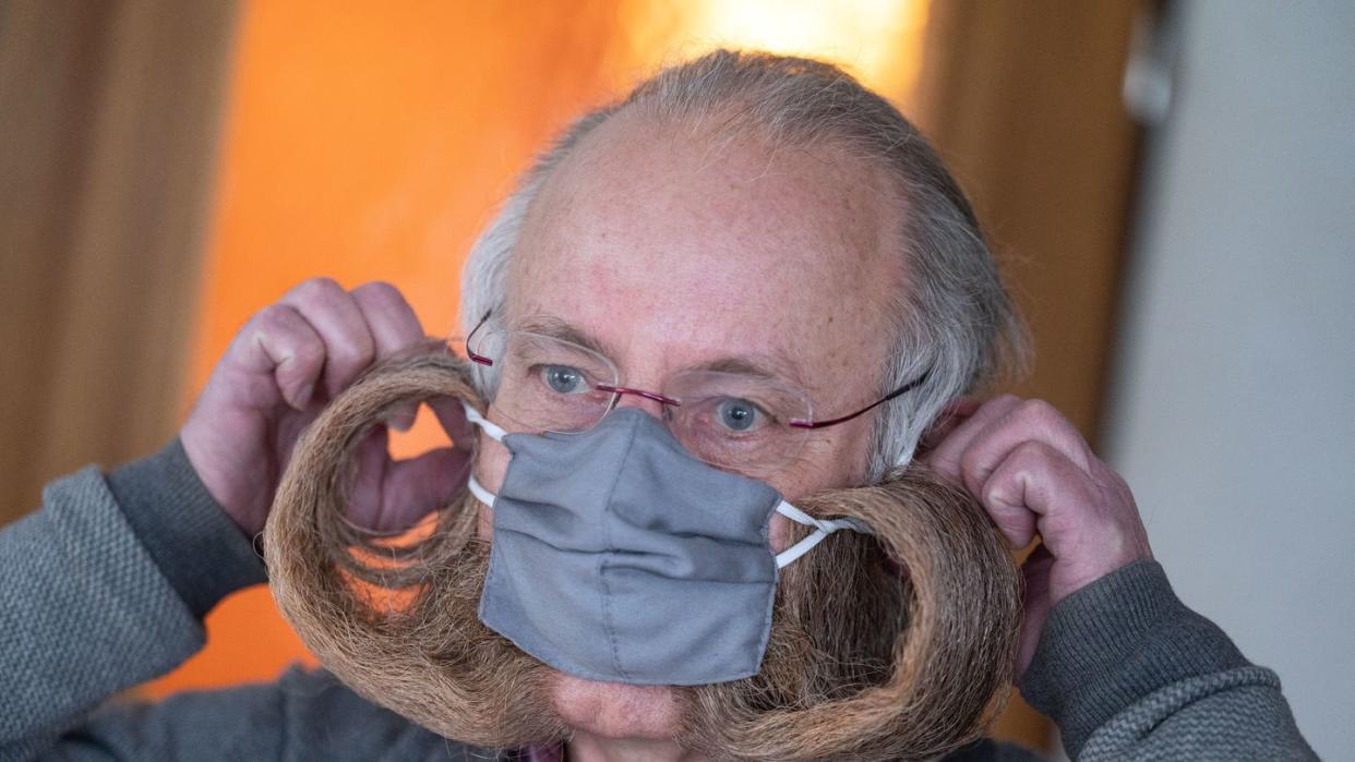 Jürgen Burkhardt, Bartträger und mehrfacher Bartweltmeister, demonstriert das Anlegen seines für ihn von einer Schneiderin angefertigten Mundschutzes.