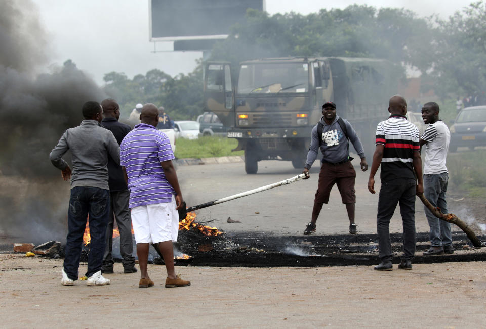 Plain clothed soldiers remove the barricade as protestors gather during a demonstration over the hike in fuel prices in Harare, Zimbabwe, Tuesday, Jan. 15, 2019. A Zimbabwean military helicopter on Tuesday fired tear gas at demonstrators blocking a road and burning tires in the capital on a second day of deadly protests after the government more than doubled the price of fuel in the economically shattered country. (AP Photo/Tsvangirayi Mukwazhi)