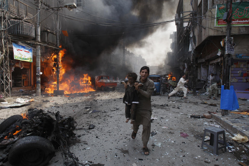 FILE - In this Sept. 29, 2013 file photo, a Pakistani man carrying a child rushes away from the site of a blast shortly after a car bomb exploded in Peshawar, Pakistan. Terror attacks in Pakistan plummeted by more than 85% over the last decade. It's a welcome statistic for the country, but one that risks being overshadowed by international concern over its efforts to curb terror funding and lingering militant activity that could test any future peace agreement in Afghanistan. (AP Photo/Mohammad Sajjad, File)