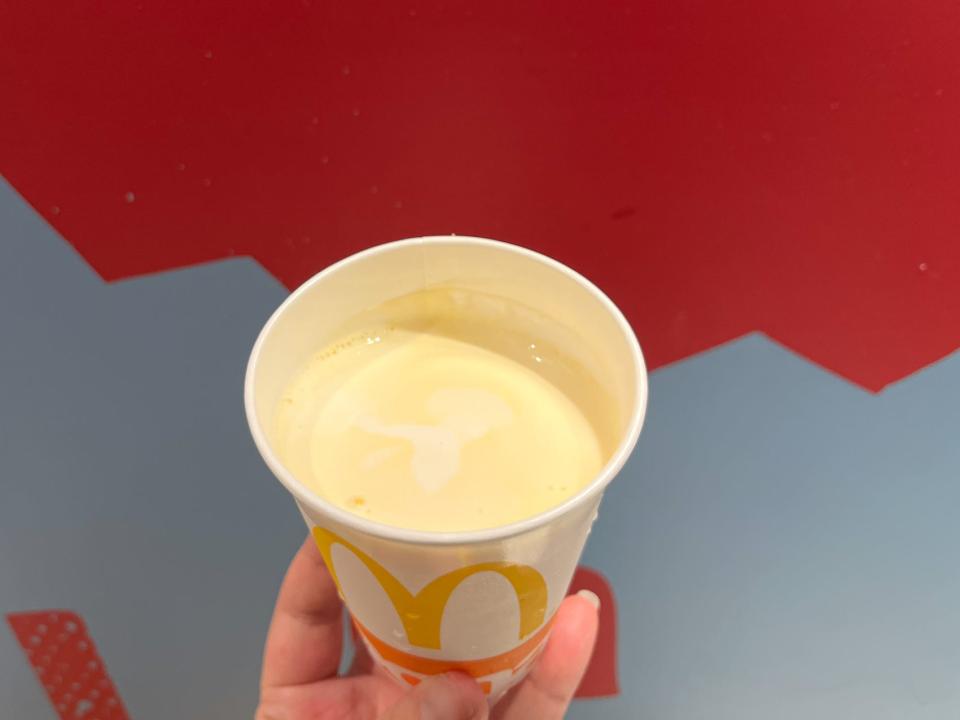 A hand holding a yellow-colored milkshake.