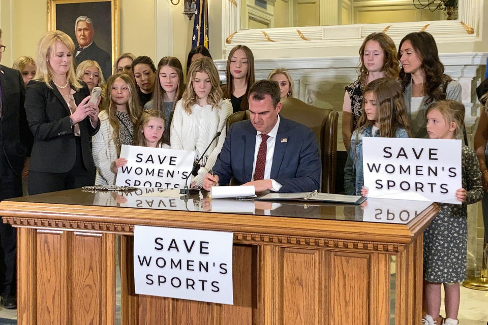 FILE - Oklahoma Gov. Kevin Stitt, center, signs a bill that prevents transgender girls and women from competing on female sports teams, March 30, 2022, in Oklahoma City. In a lawsuit filed Monday, April 29, 2024, four Republican state attorneys general are challenging a federal regulation that seeks to protect the rights of transgender students in the nation's schools by banning blanket policies that bar transgender students from school bathrooms aligning with their gender, among other provisions. (AP Photo/Sean Murphy, File)