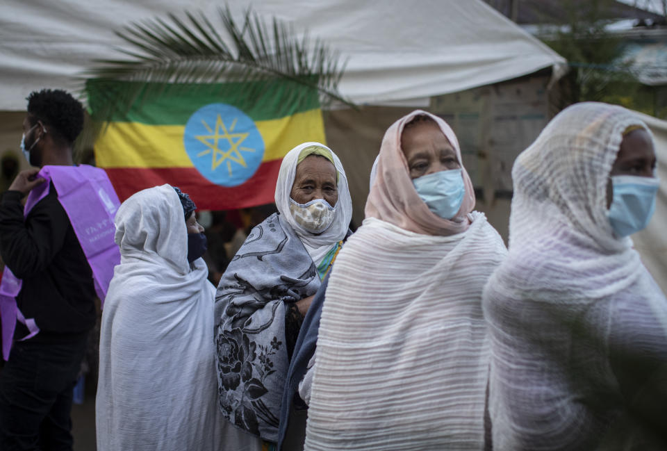 Ethiopians queue to cast their votes in the general election, next to a national flag, at a polling center in the capital Addis Ababa, Ethiopia, Monday, June 21, 2021. Ethiopia was voting Monday in the greatest electoral test yet for Prime Minister Abiy Ahmed as insecurity and logistical issues meant ballots wouldn't be cast in more than 100 constituencies of the 547 across the country. (AP Photo/Ben Curtis)