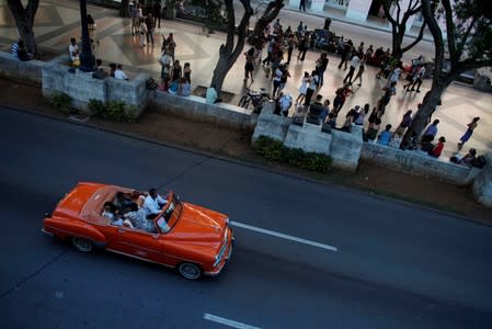 A vintage car with tourists pass by as people dance tango during a weekly Sunday milonga on Havana's Paseo del Prado promenade