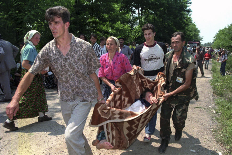 FILE- In this Thursday, July 13, 1995, file picture, refugees and a Bosnian government soldier carry a sick woman on a makeshift stretcher to a hospital inside a U.N. base outside Tuzla. Survivors of the genocide in the eastern Bosnian town of Srebrenica, mainly women, will on Saturday July 11, 2020, commemorate the 25th anniversary of the slaughter of their fathers and brothers, husbands and sons. (AP Photo/Darko Bandic, File)