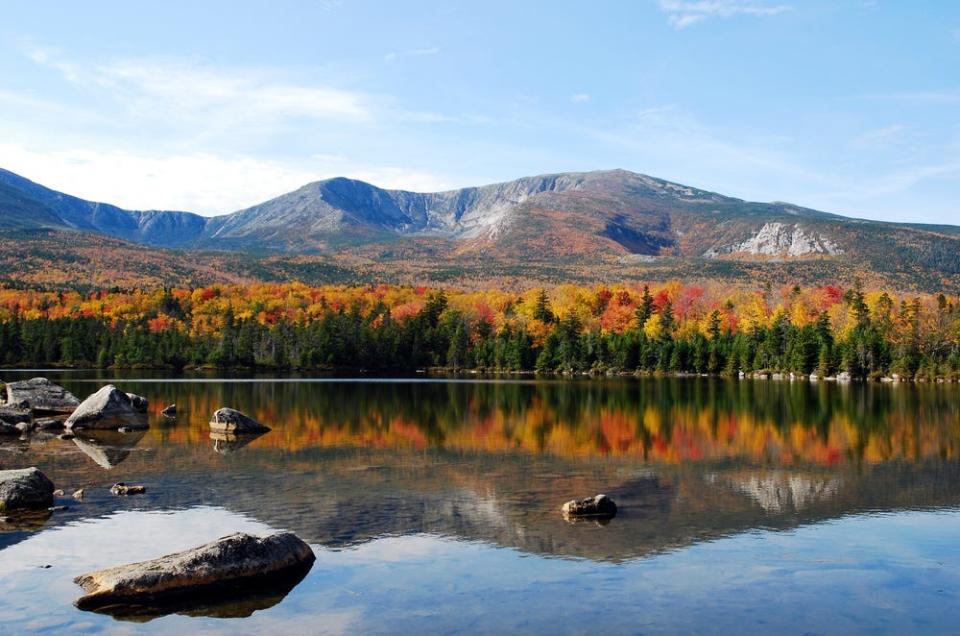 A large mountain and fall-colored trees line a pond.