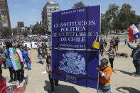 In this Nov. 12, 2019 photo, anti-government demonstrators carry a sign representing Chile's Constitution during protests, in Santiago, Chile. In 1981, during the dictatorship of Augusto Pinochet, Chile enacted a pension system that requires all workers to allocate 10% of their earnings to privately run pension fund administrators, known by their Spanish initials of AFP. Those who haven’t made contributions, or have very few, receive a basic pension from the state that amounts to $146 a month. That minimum wasn’t introduced until 2008 under the government of Michelle Bachelet, and later modified in response to public demands. (AP Photo/Esteban Felix)