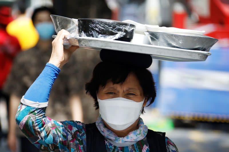 A restaurant worker carring a meal on her head walks on Myeongdong shopping district which is nearly empty amid the coronavirus disease (COVID-19) pandemic in Seoul